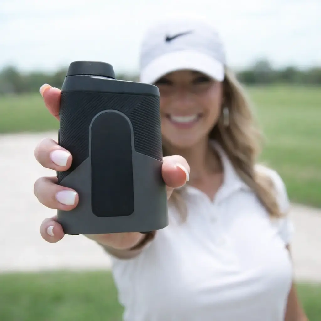 Female golfer in white polo and cap holding a compact golf rangefinder on the course